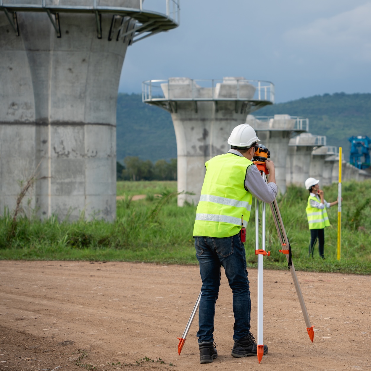 Survey team is working with a theodolite and road construction plans. Civil engineers are taking measurements with surveying tools during the construction.